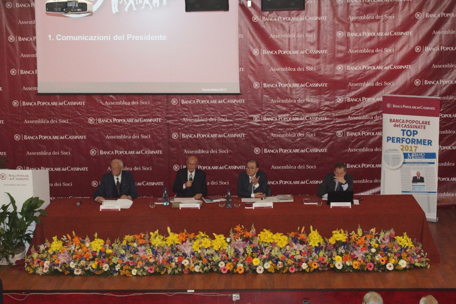 Conferenza stampa con relatori al tavolo e fiori colorati sul palco.