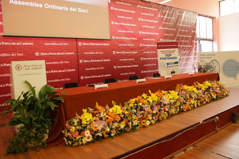 Palco allestito per l'Assemblea Ordinaria dei Soci con fiori e pannelli informativi.