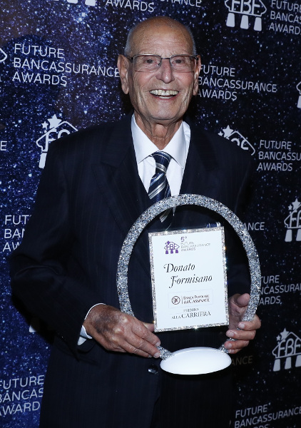Uomo anziano sorridente con un premio in mano.
