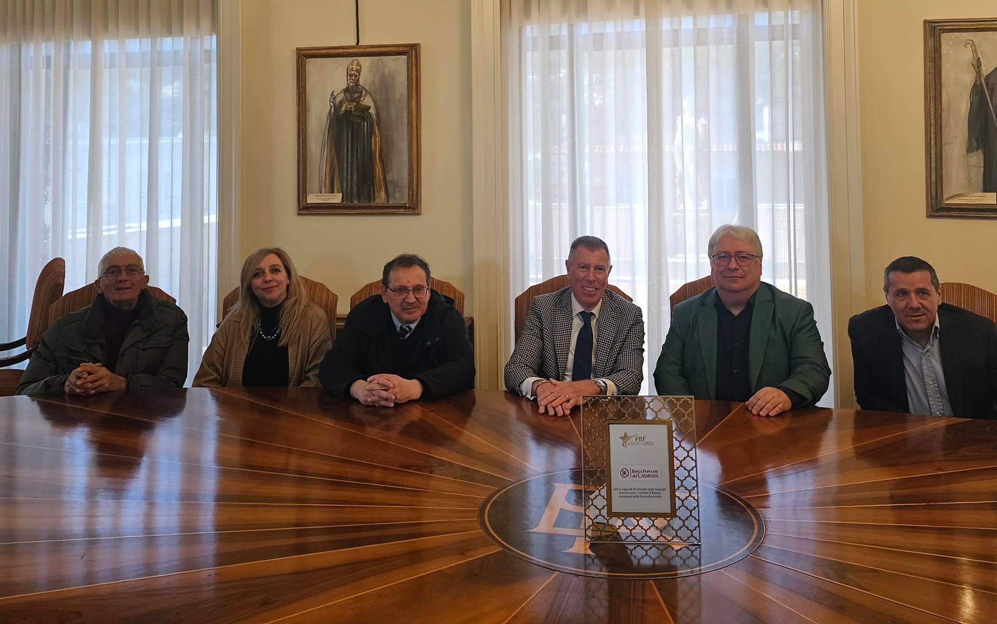 Gruppo di persone sedute attorno a un tavolo in una sala con finestre e decorazioni.