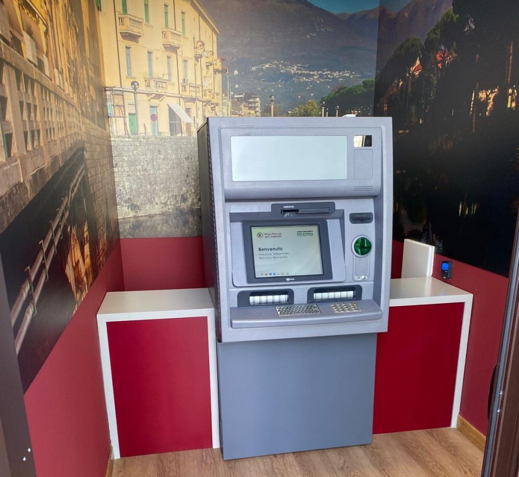 Un bancomat moderno situato in un ambiente interno con pareti decorate e mobili rossi.